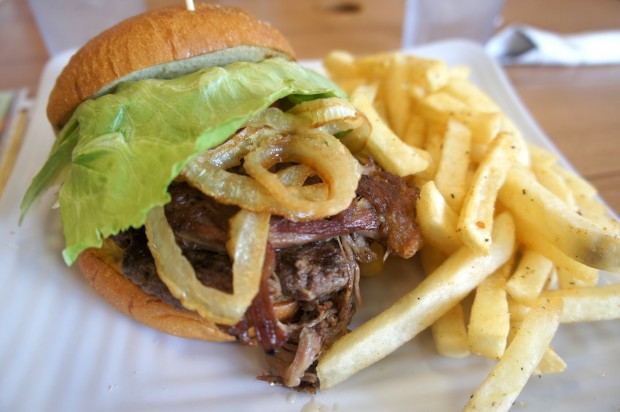  Ali'i burger, consisting of a juicy 1/4 pound burger patty topped with crispy kalua pulled pork and pineapple BBQ sauce on a brioche bun with a side of fries